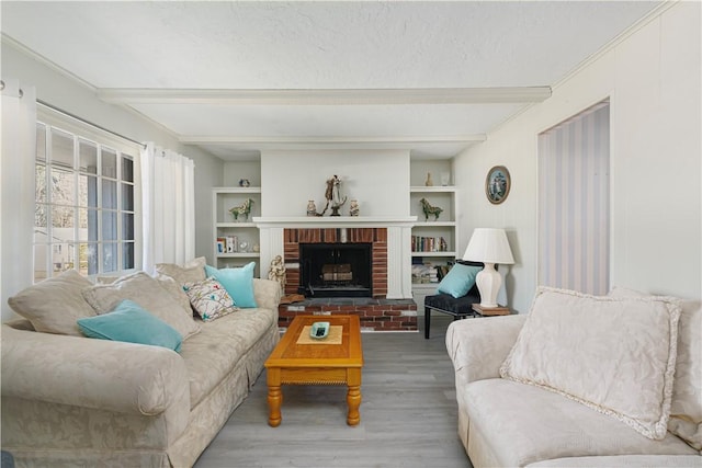 living room with a textured ceiling, beamed ceiling, a brick fireplace, and wood finished floors