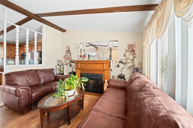 living area featuring lofted ceiling with beams, light wood finished floors, and a glass covered fireplace