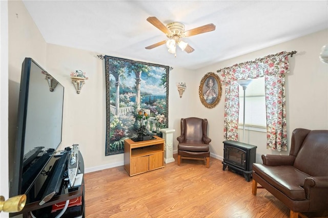 living area featuring a wood stove, ceiling fan, light wood-style flooring, and baseboards