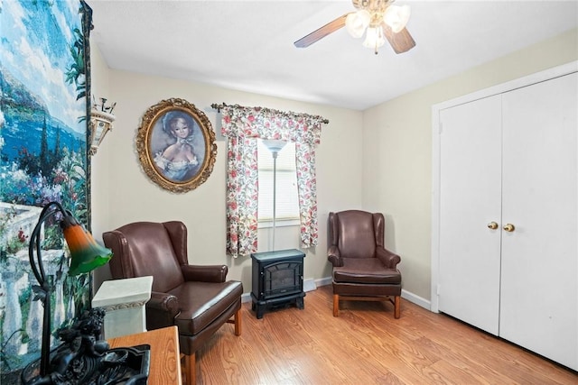 living area featuring a wood stove, ceiling fan, baseboards, and wood finished floors