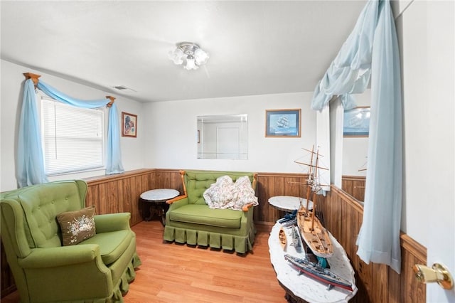 living area with wainscoting, wood finished floors, visible vents, and wooden walls