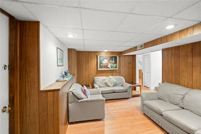 living room with light wood-style flooring, wood walls, a drop ceiling, and visible vents