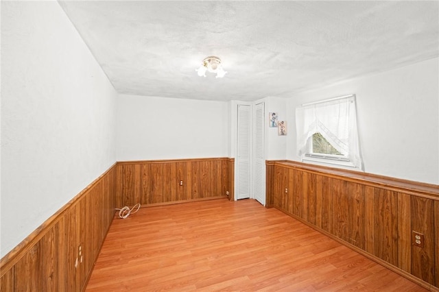 unfurnished room featuring a wainscoted wall, a textured ceiling, light wood-type flooring, and wooden walls