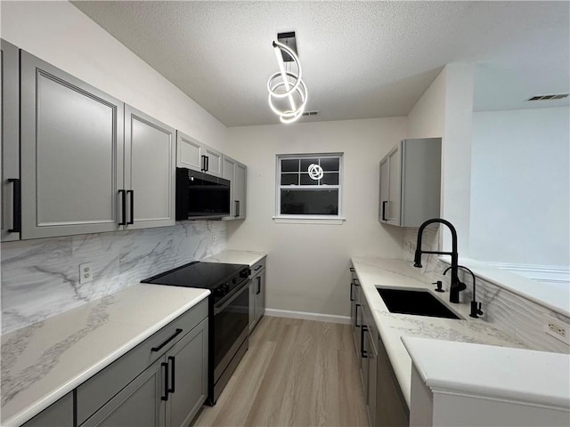 kitchen featuring gray cabinets, visible vents, light wood-style flooring, a sink, and black appliances