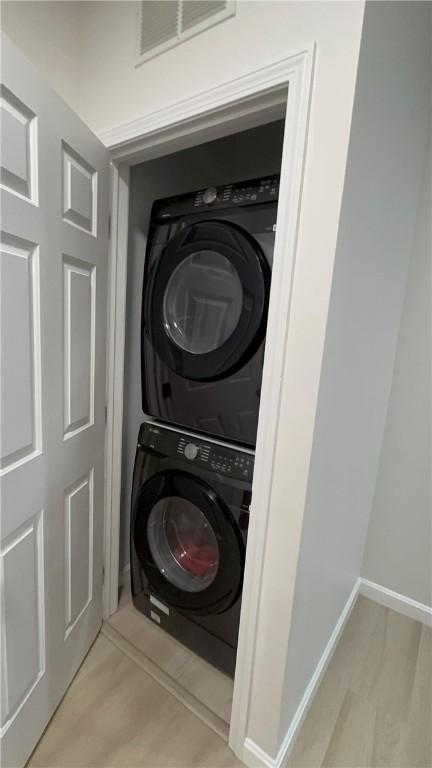 laundry room with stacked washer / dryer, laundry area, light wood-style flooring, and baseboards