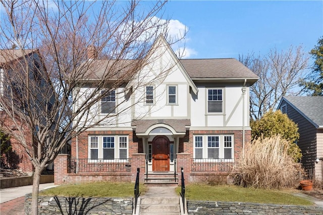 tudor home with a shingled roof, brick siding, and stucco siding