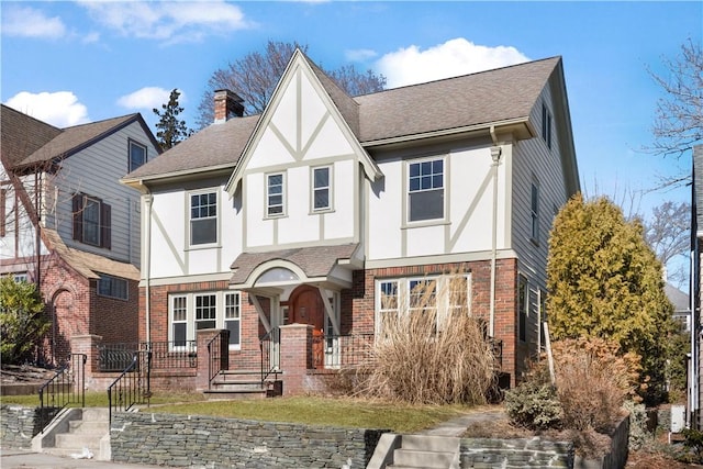 tudor house featuring brick siding, a chimney, a shingled roof, and stucco siding