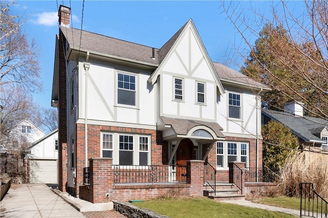 tudor-style house featuring brick siding, a chimney, a porch, and stucco siding