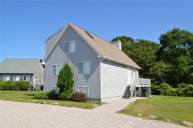 view of side of property featuring a chimney, stairway, a deck, and a lawn