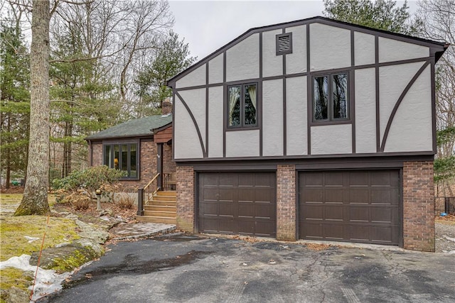 tudor-style house featuring driveway, brick siding, a garage, and stucco siding