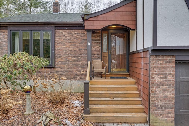 entrance to property featuring a garage, brick siding, and a chimney