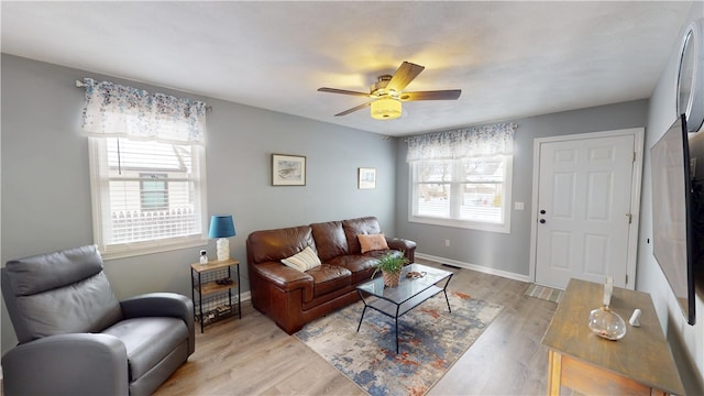 living room featuring light wood-type flooring, a ceiling fan, baseboards, and a wealth of natural light