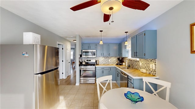 kitchen featuring appliances with stainless steel finishes, a sink, light countertops, blue cabinetry, and backsplash