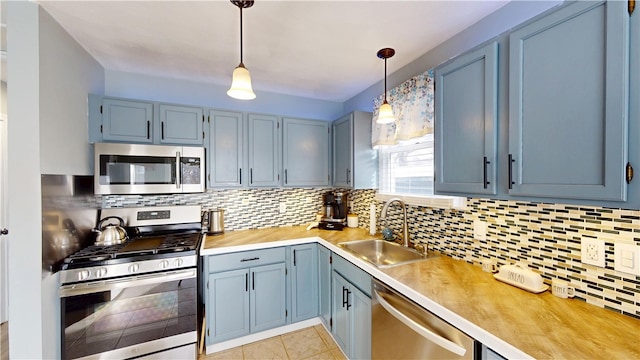 kitchen featuring appliances with stainless steel finishes, light countertops, a sink, and decorative light fixtures