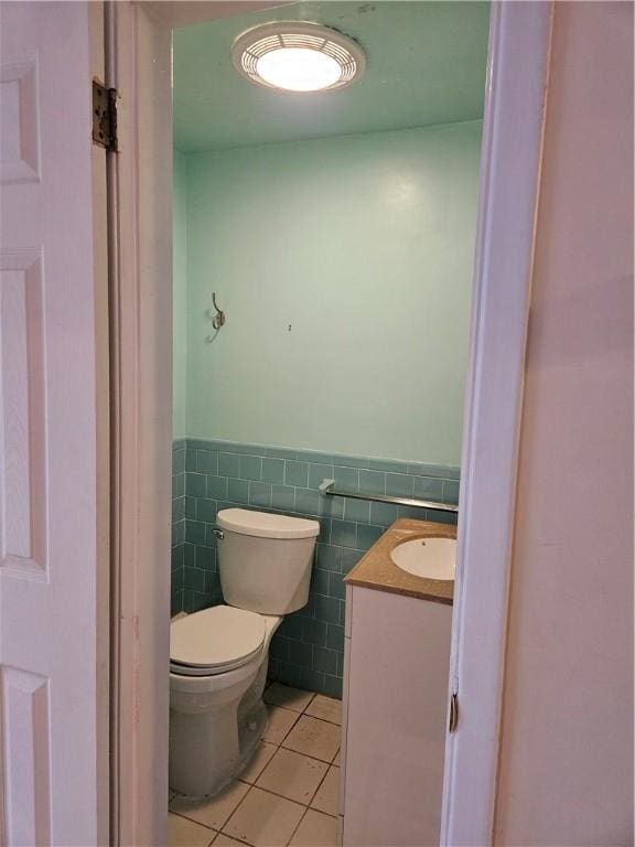 half bath featuring a wainscoted wall, tile walls, toilet, vanity, and tile patterned flooring