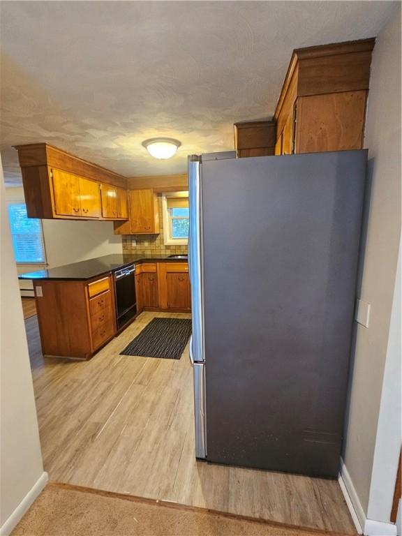 kitchen with light wood-style flooring, freestanding refrigerator, brown cabinets, dishwasher, and dark countertops