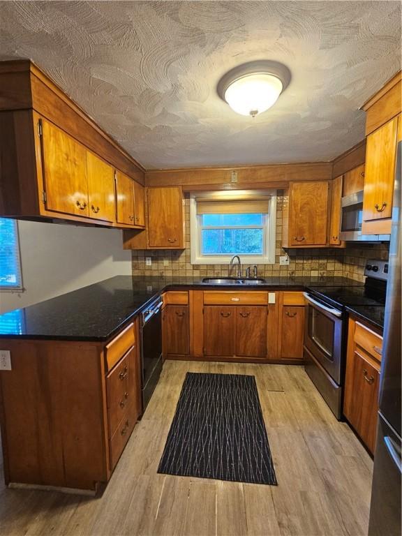 kitchen with stainless steel appliances, brown cabinetry, dark countertops, and a sink