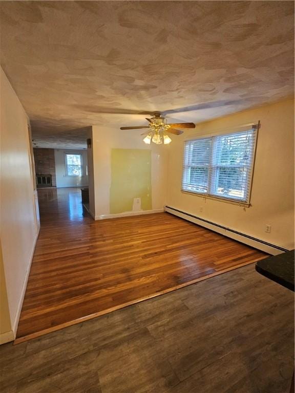 unfurnished room with a baseboard heating unit, wood finished floors, a ceiling fan, and baseboards