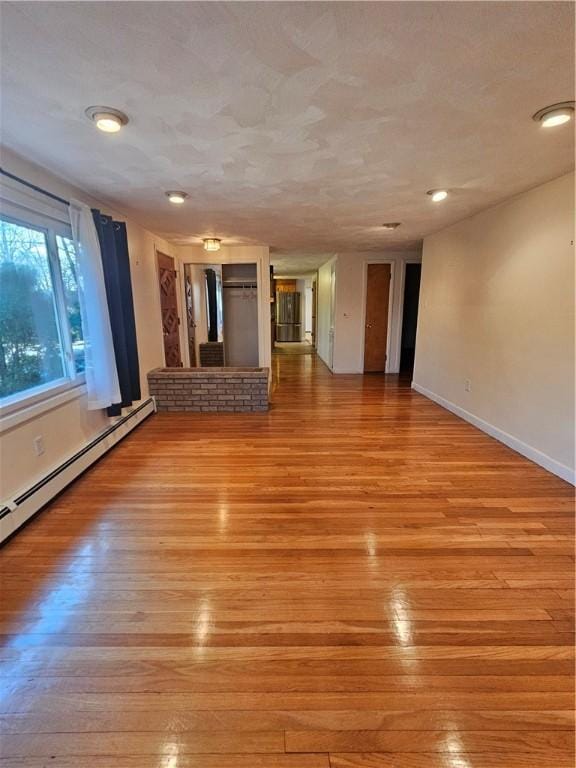 spare room featuring a baseboard heating unit, light wood-style flooring, and baseboards