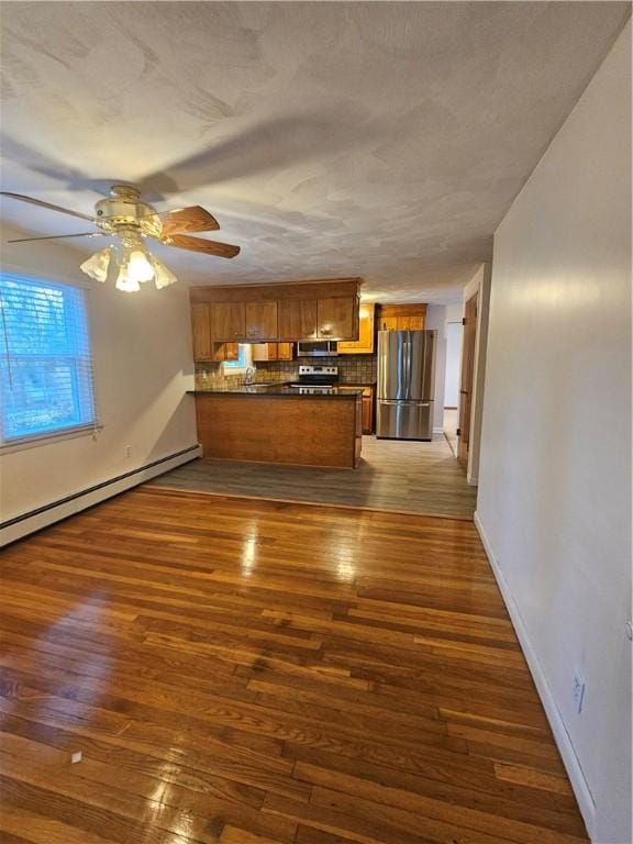 kitchen with brown cabinetry, dark wood finished floors, dark countertops, a peninsula, and stainless steel appliances