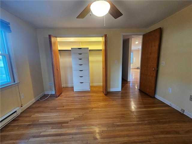 unfurnished bedroom featuring a closet, baseboards, baseboard heating, and wood finished floors