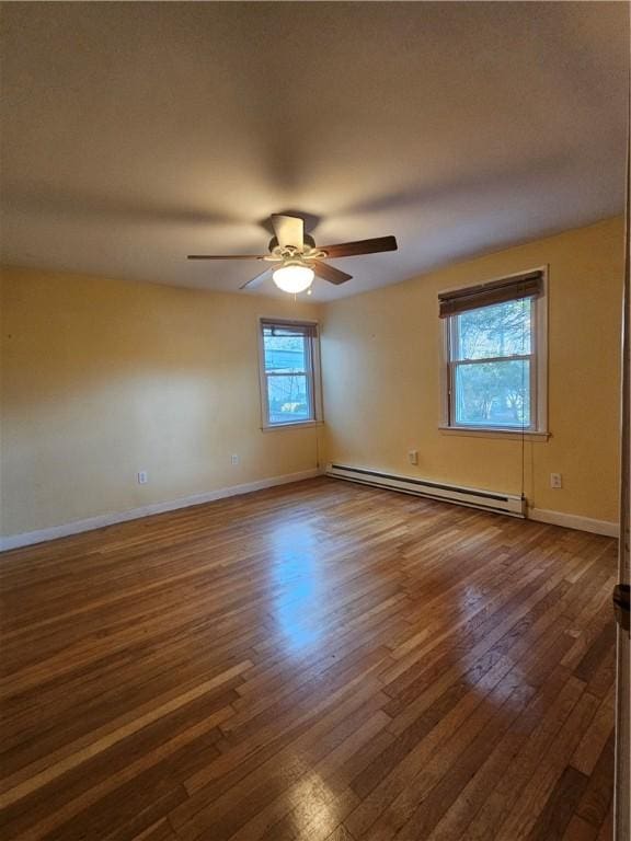 spare room featuring dark wood-style floors, ceiling fan, a baseboard heating unit, and baseboards