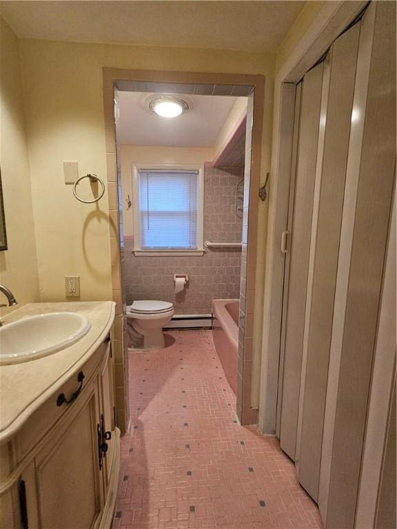 bathroom with a baseboard radiator, toilet, a bathing tub, vanity, and tile walls