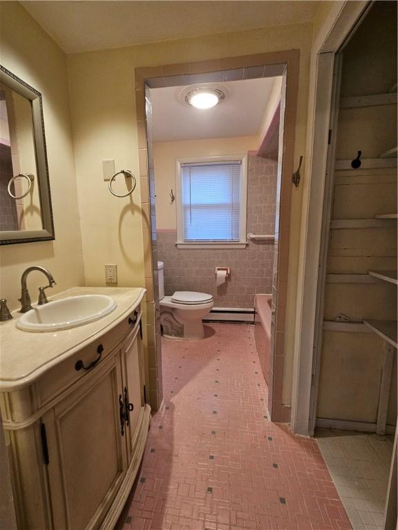 bathroom with toilet, tile walls, vanity, baseboard heating, and a tub