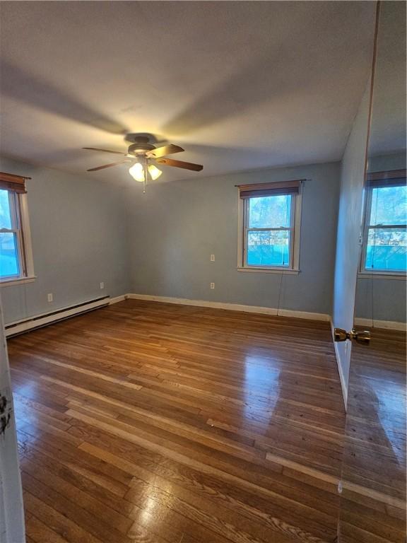 spare room with a baseboard radiator, wood-type flooring, and a healthy amount of sunlight