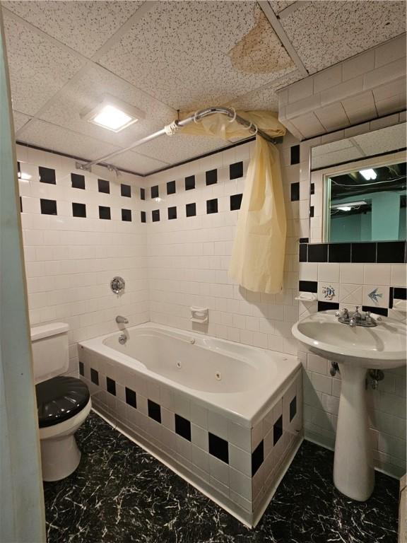 bathroom featuring a combined bath / shower with jetted tub, marble finish floor, tile walls, and toilet