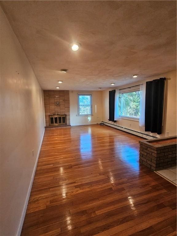 unfurnished living room featuring a baseboard radiator, plenty of natural light, wood-type flooring, and baseboards