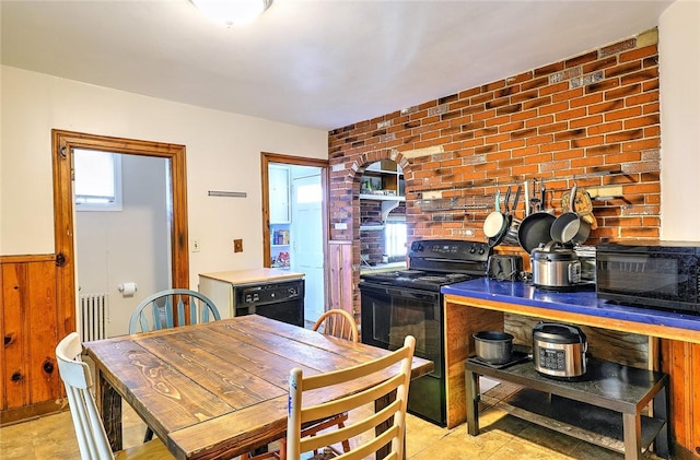 kitchen with brick wall, a wainscoted wall, and black appliances