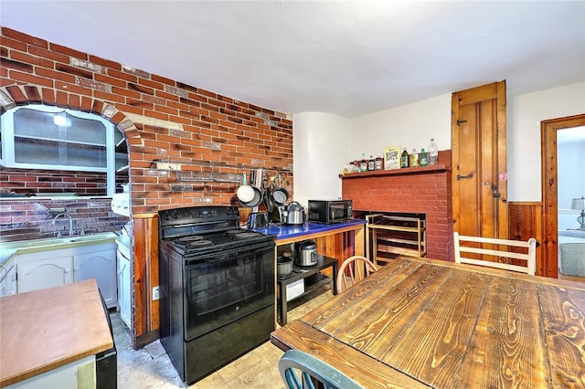 kitchen featuring brick wall, a sink, a fireplace, and black appliances