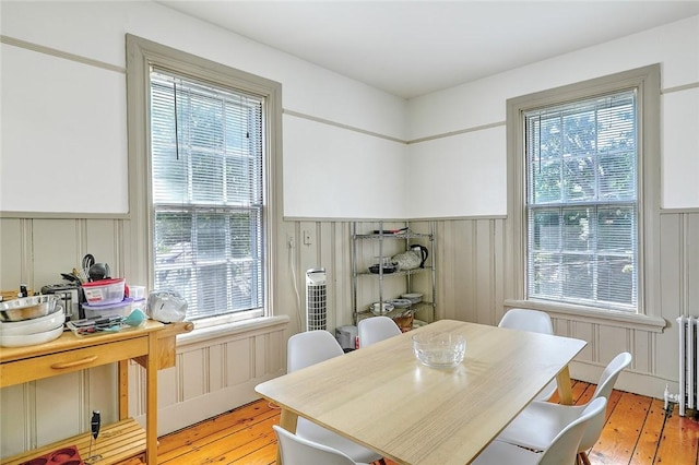 dining area featuring light wood-type flooring, a decorative wall, and radiator heating unit