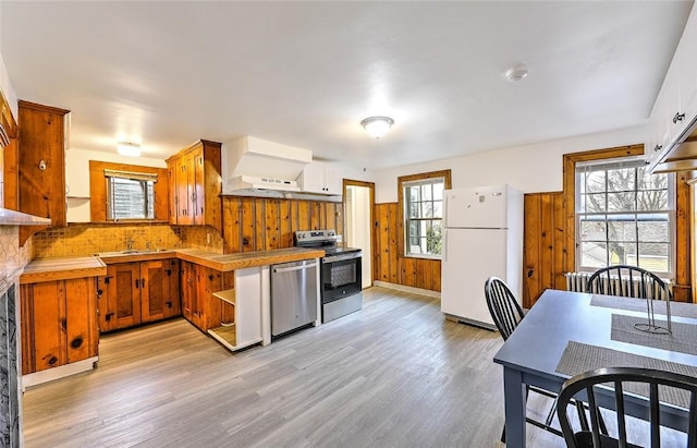 kitchen featuring stainless steel appliances, light countertops, light wood-type flooring, wood walls, and a sink