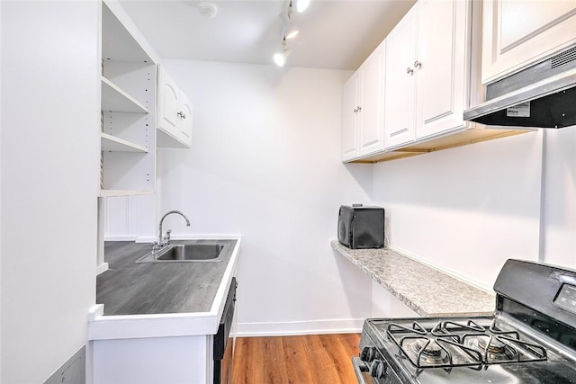 kitchen with light wood-style flooring, under cabinet range hood, a sink, white cabinets, and range with gas stovetop