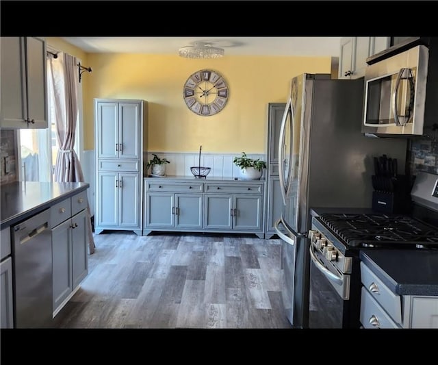 kitchen with stainless steel appliances, backsplash, dark countertops, and wood finished floors