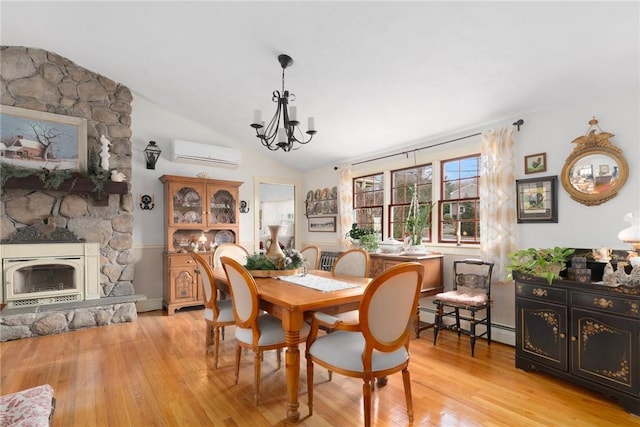 dining area with a wall unit AC, a fireplace, baseboard heating, light wood-style floors, and vaulted ceiling