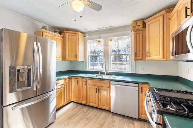 kitchen featuring light wood-style flooring, appliances with stainless steel finishes, a ceiling fan, a sink, and a textured ceiling