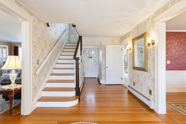 entryway with a baseboard radiator, wallpapered walls, wood finished floors, baseboards, and stairs