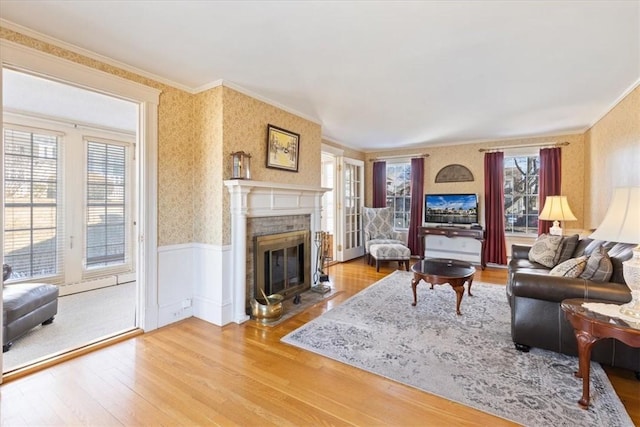 living area with wallpapered walls, crown molding, wood finished floors, and wainscoting