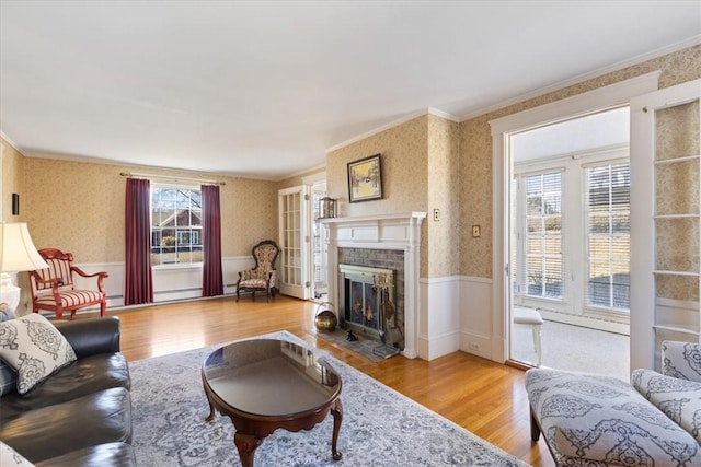 living area with a wainscoted wall, crown molding, wood finished floors, a tile fireplace, and wallpapered walls