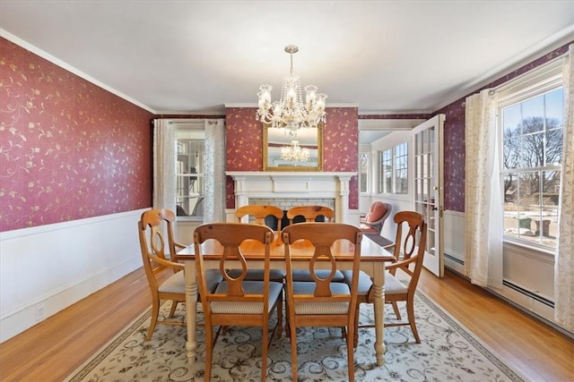 dining room with light wood-style floors, wainscoting, crown molding, and wallpapered walls