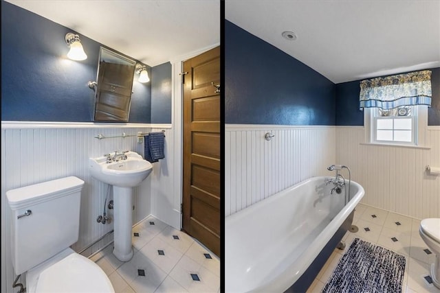 full bath with a wainscoted wall, a freestanding bath, toilet, a sink, and tile patterned flooring