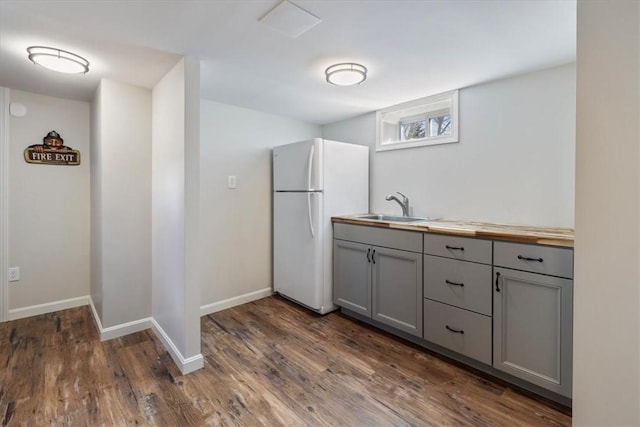 kitchen with dark wood-style flooring, gray cabinetry, freestanding refrigerator, a sink, and baseboards