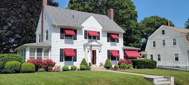 colonial house featuring a shingled roof, a chimney, and a front yard