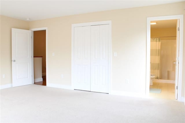 unfurnished bedroom featuring carpet floors, a closet, baseboards, and ensuite bathroom