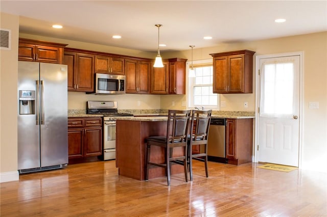 kitchen with recessed lighting, a breakfast bar, wood finished floors, appliances with stainless steel finishes, and pendant lighting