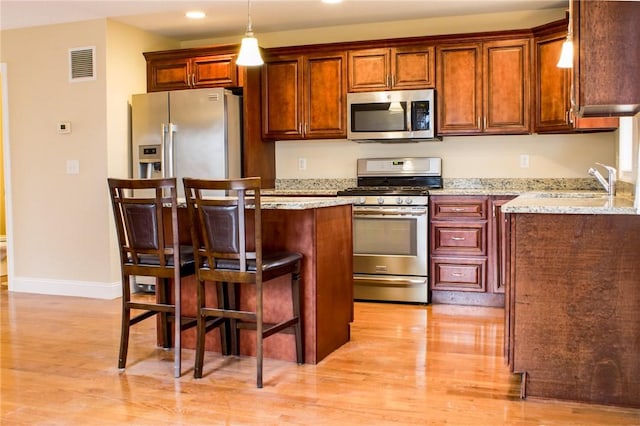 kitchen with stainless steel appliances, a breakfast bar, visible vents, light wood-type flooring, and a center island