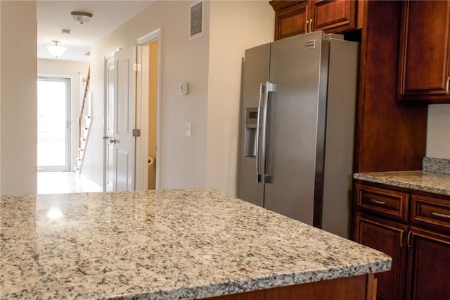 kitchen featuring visible vents, stainless steel fridge with ice dispenser, and light stone countertops